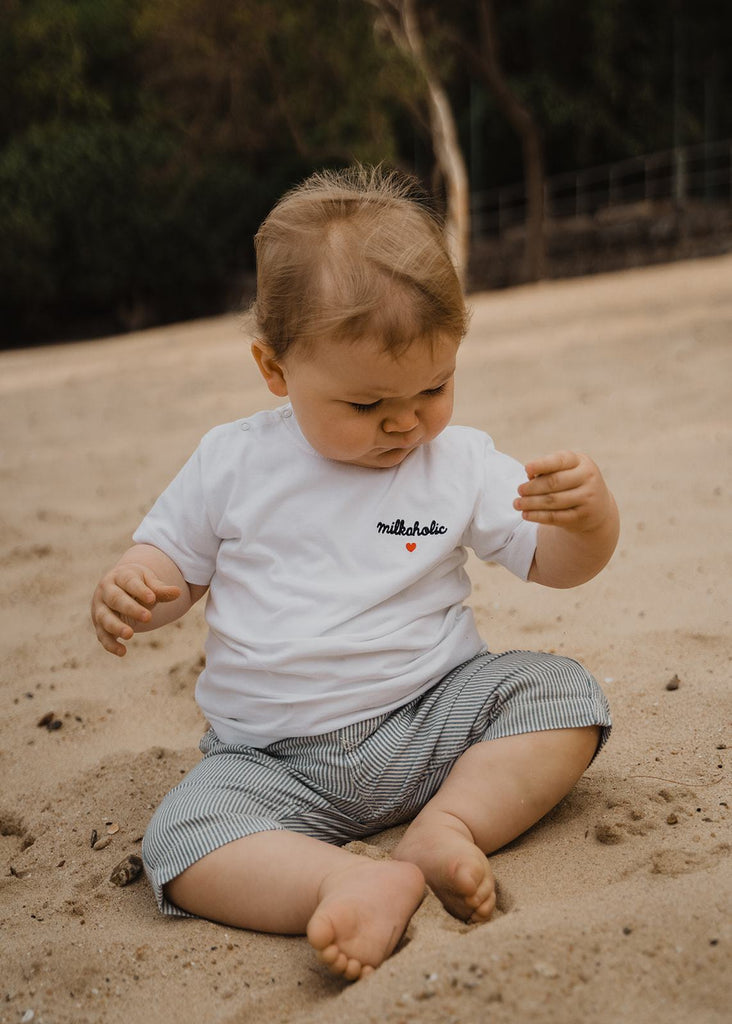 Our organic baby t-shirt “Milkaholic“ made of 100% premium organic cotton with 2 snap buttons on the right shoulder. Our baby t-shirts are soft like a cocoon! The baby t-shirt is white and has a navy blue embroidery “Milkaholic” with a red heart - on the left side - close to the heart.