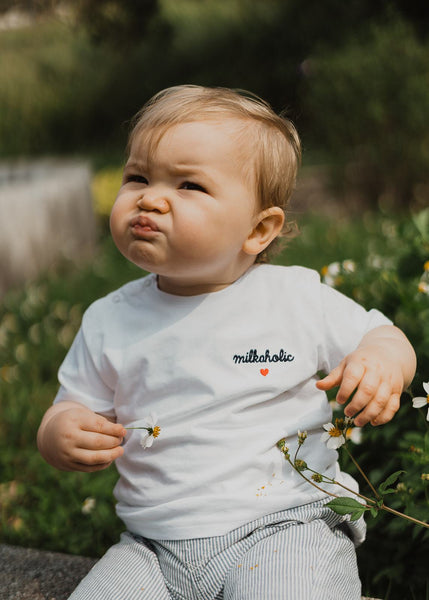 Our organic baby t-shirt “Milkaholic“ made of 100% premium organic cotton with 2 snap buttons on the right shoulder. Our baby t-shirts are soft like a cocoon! The baby t-shirt is white and has a navy blue embroidery “Milkaholic” with a red heart - on the left side - close to the heart.